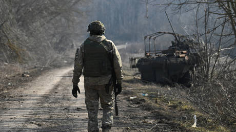 A Russian serviceman of the Sever (North) group of forces walks past a burned-out Ukrainian BTR-4 Bucephalus armoured personnel carrier (APC)